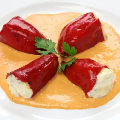 Cuatro pimientos rojos rellenos de bacalao, servidos sobre una cremosa salsa naranja y decorados con perejil.