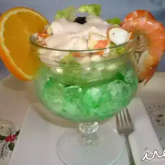 Delicioso coctel de marisco servido en copa con hielo verde, adornado con naranja y gamba.
