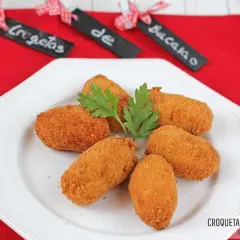 Seis croquetas de bacalao doradas y crujientes, adornadas con perejil fresco, servidas en un plato blanco.