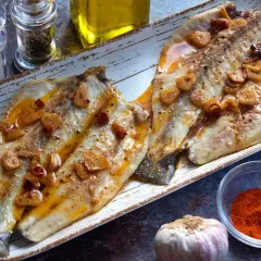 Dos filetes de lubina a la bilbaina, dorados y jugosos, con láminas de ajo crujiente y guindilla.