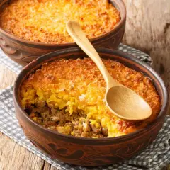 Dos cazuelas de barro con pastel de choclo, una con cuchara de madera. Un plato chileno casero y delicioso.