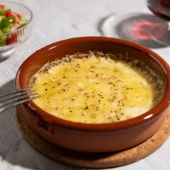 Delicioso provolone al horno burbujeante, servido en cazuela de barro con una guarnición de pimientos y una copa de vino tinto.