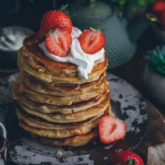 Pila de tortitas esponjosas cubiertas con nata y fresas. Una deliciosa receta de tortitas para el desayuno.