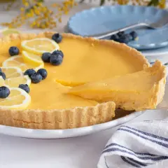 Deliciosa tarta de limón, decorada con rodajas de limón y arándanos. Una porción se sirve con una espátula.