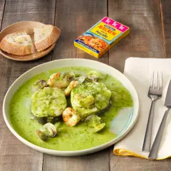 Merluza a la vasca con gambas y almejas en salsa verde, acompañada de pan.