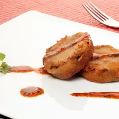 Dos porciones de manitas de cerdo rebozadas y fritas, servidas con salsa roja y perejil en un plato blanco.