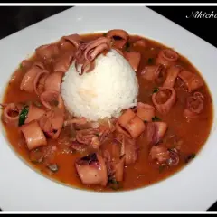 Calamares encebollados en una salsa rojiza, servidos con una bola de arroz blanco en un plato blanco.