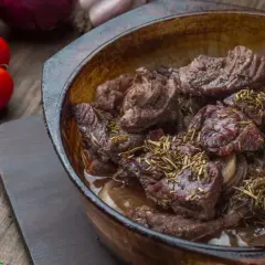 Carrilleras de ternera estofadas con romero y cebolla, servidas en cazuela de barro.