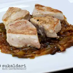 Cuatro trozos de bonito encebollado, jugosos y dorados, reposan sobre una cama de cebolla caramelizada y pimientos verdes.