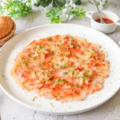 Delicioso carpaccio de gambas con aderezo y hierbas frescas, servido con panecillos.
