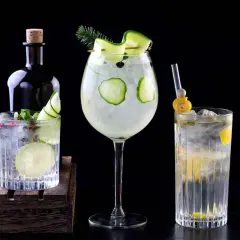 Tres refrescantes cócteles de ginebra, decorados con pepino y limón, junto a una botella de ginebra.