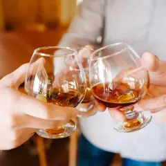 Manos brindando con copas de brandy ámbar. ¿Qué es el brandy? Es un espíritu destilado de vino, perfecto para celebrar.