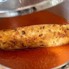 Rollo de bonito dorado y crujiente nadando en una salsa de tomate casera, listo para ser servido.