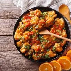 Delicioso pollo a la naranja, crujiente y bañado en una salsa dulce y cítrica, adornado con cebollín fresco.