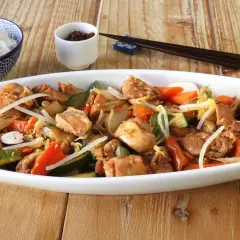 Un delicioso chop suey de pollo con verduras y brotes de soja, servido en un plato blanco junto a un tazón de arroz blanco y palillos.