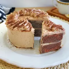 Deliciosa tarta de moka con crema y cacao espolvoreado. Un trozo cortado revela sus capas de bizcocho y relleno.