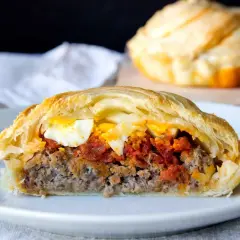 Un trozo de pastel de carne murciano, relleno de carne picada, tomate y huevo duro, envuelto en hojaldre dorado.