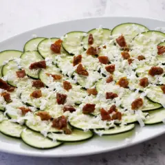 Carpaccio de calabacín fresco, adornado con queso rallado y trocitos de tomate seco. Un plato ligero y lleno de sabor.