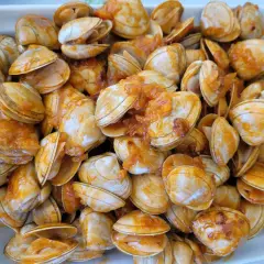 Un plato rebosante de almejas a la marinera, con su salsa anaranjada cubriendo las conchas.