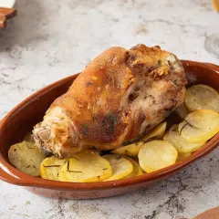Codillo de cerdo asado, crujiente y dorado, servido en cazuela de barro con patatas panadera.
