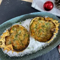 Dos deliciosos txangurros a la donostiarra, gratinados y espolvoreados con perejil, reposan sobre sal gruesa en un plato festivo.