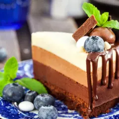 Deliciosa tarta tres chocolates en un plato azul, decorada con arándanos y menta.
