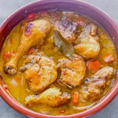 Sabroso pollo en salsa con trozos dorados, zanahorias y laurel en una cazuela de barro.