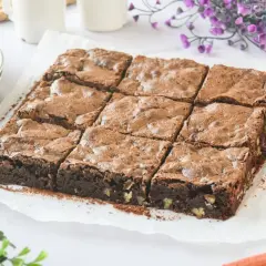 Un delicioso brownie sin gluten, cortado en nueve porciones, espolvoreado con cacao y con trozos de nuez visibles.