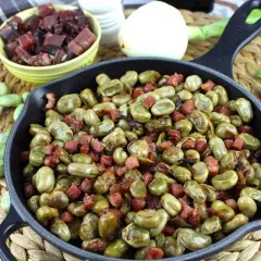 Habitas tiernas salteadas con trocitos de jamón crujiente en una sartén de hierro fundido. Un plato casero y delicioso.