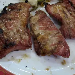 Tres jugosas porciones de secreto ibérico a la parrilla, con sal gruesa y un toque de pimienta, servidas en un plato blanco con borde decorado.