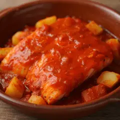 Bacalao a la riojana, un plato tradicional con trozos de patata y pimiento en una salsa roja sabrosa, servido en cazuela de barro.