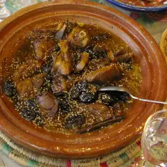 Un delicioso tajine de cordero con ciruelas pasas y semillas de sésamo, servido en una cazuela de barro.