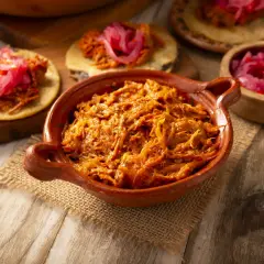 Cochinita pibil en cazuela de barro, lista para servir en tortillas con cebolla morada encurtida. ¡Un festín de sabor!