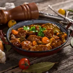 Un delicioso caldereta de cordero, con trozos tiernos de carne, zanahorias y brócoli, servido en una cazuela rústica.