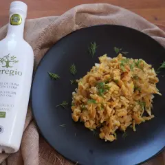 Un plato de revuelto de bacalao con eneldo fresco, acompañado de una botella de aceite de oliva virgen extra ecológico Egregio.