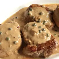 Cuatro medallones de solomillo a la pimienta, cubiertos con una cremosa salsa de pimienta verde, servidos en un plato blanco.