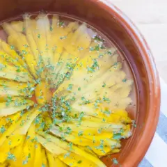 Boquerones en vinagre dispuestos en círculo en una cazuela de barro, espolvoreados con perejil picado.