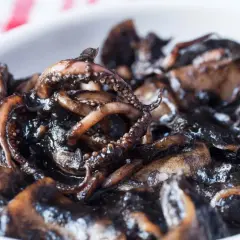 Un plato de calamares en su tinta, con tentáculos visibles y una salsa oscura y brillante.