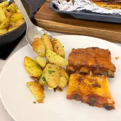 Costillas de churrasco al horno con patatas asadas y hierbas.