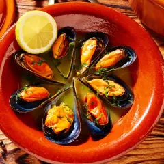 Mejillones al vapor servidos en un cuenco de barro con limón y perejil.