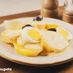 Papa a la huancaina servida en un plato blanco, con rodajas de huevo duro y aceitunas negras.