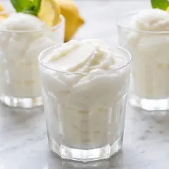 Tres vasos de sorbete de limón refrescante, con limones amarillos y hojas de menta en el fondo.