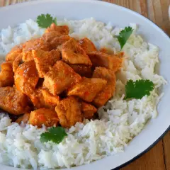 Sabroso pollo tikka masala cubierto con arroz blanco y decorado con cilantro fresco.