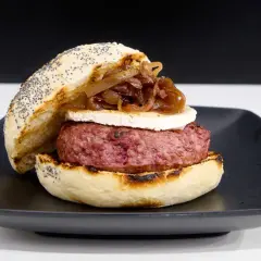 Deliciosa hamburguesa de ternera con queso de cabra y cebolla caramelizada, servida en pan con semillas de amapola.
