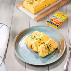 Rebanadas de pastel de pescado, esponjoso y dorado, servido en plato azul. Acompañado de un caldo de pescado.