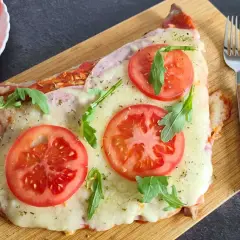 Un delicioso matambre a la pizza, cubierto de queso derretido, rodajas de tomate fresco y rúcula, servido en tabla de madera.