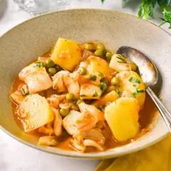 Un plato humeante de patatas con sepia de la abuela, con guisantes y perejil fresco.