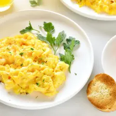 Un plato de huevos revueltos esponjosos, adornado con perejil fresco y acompañado de tostadas crujientes.
