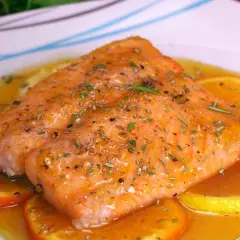 Delicioso salmón a la naranja, bañado en salsa cítrica y adornado con rodajas de naranja y hierbas frescas.