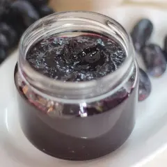 Frasco de mermelada de uvas casera, con uvas frescas al lado. Un dulce manjar para disfrutar.